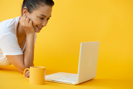 Woman is using white laptop on the yellow background.