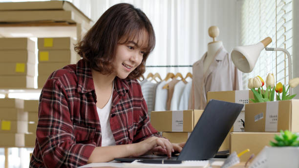 istock Young asia people woman female e-commerce parcel work check typing talk to customer on notebook for box shipping online fulfillment sme dropshipping digital dispatch app clothes fashion supply chain. 1323528452