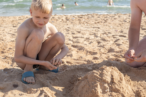 A blond boy on the beach with his father are building a tower out of sand. Summer family vacation on the seashore.