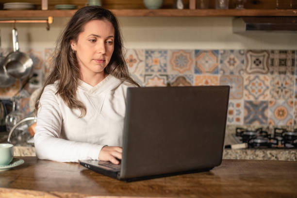 istock Woman working on laptop in the kitchen - home office concept 1323529072