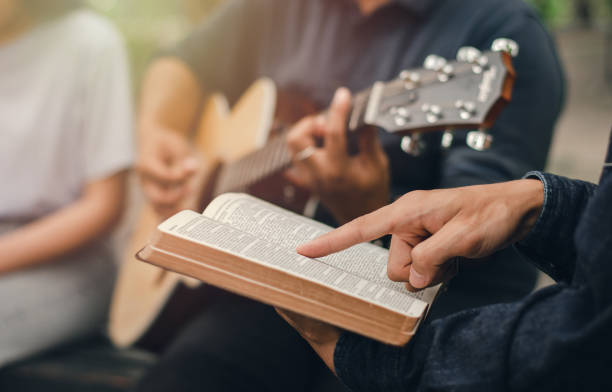 ein kleiner junge liest die bibel, während sein freund gitarre spielt. wenn er gott anbetet eine kleine gruppe von christen oder konzepte in einer kirche in einer kirche. - evangelium stock-fotos und bilder