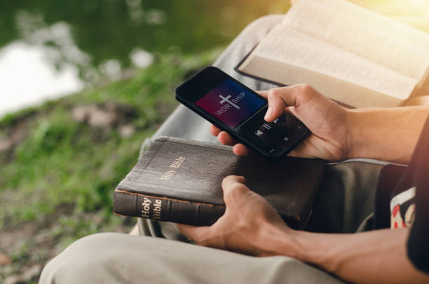 two young people searching the bible on their smartphones. ready to study the bible in the teachings of god. in the peace of nature christian family - teachings imagens e fotografias de stock