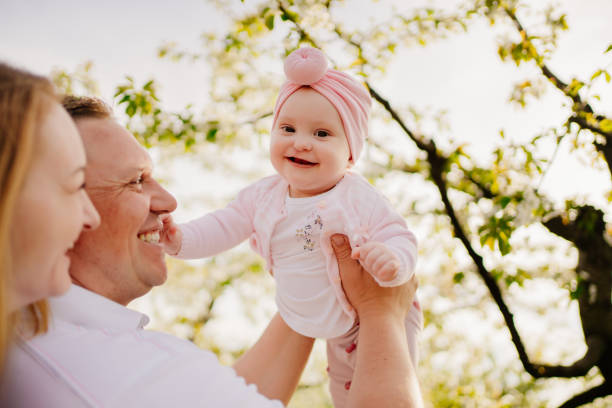 mom, dad and daughter in spring flowering garden. cleft lip in infants. mom, dad and daughter. family happiness. a family with a baby daughter in the spring flowering garden. walking and relaxing with the children. cleft lip in infants after surgery. cleft lip stock pictures, royalty-free photos & images