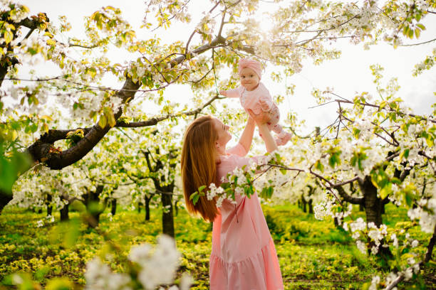 mother with baby in arms in flowering garden. surgery for child with cleft lip. mother with baby daughter in her arms in the flowering spring garden. surgery for a child with a cleft lip. Children's surgery and medicine. walks with children. happy childhood. beauty and love. cleft lip stock pictures, royalty-free photos & images