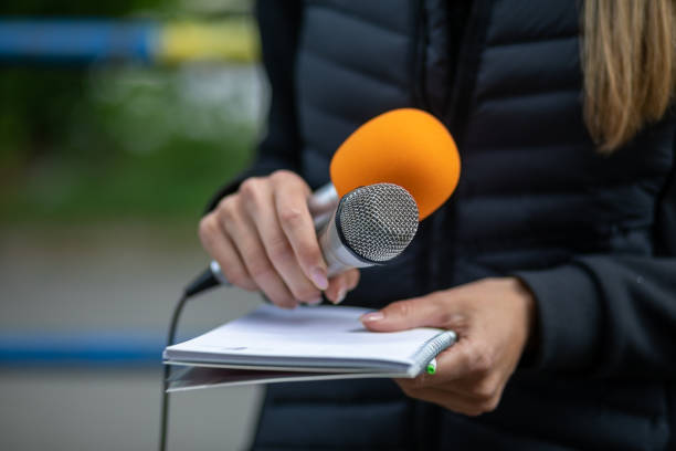 istock Journalist at news conference, writing notes, holding microphones 1323535420