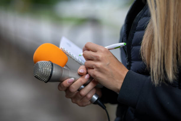 istock Journalist at news conference, writing notes, holding microphones 1323535449