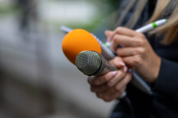 istock Journalist at news conference, writing notes, holding microphones 1323535503