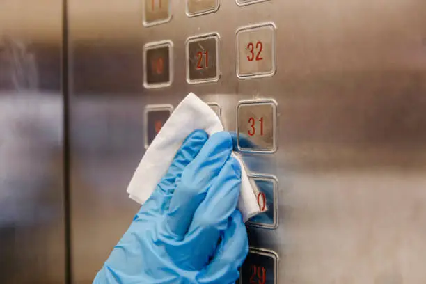 Hands with protective gloves wiping down push button in elevator