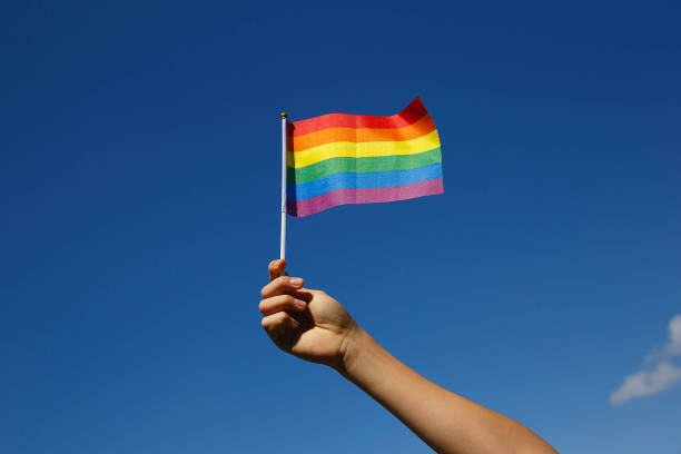 piccola bandiera lgbt in mano contro il cielo blu - gay pride wristband rainbow lgbt foto e immagini stock