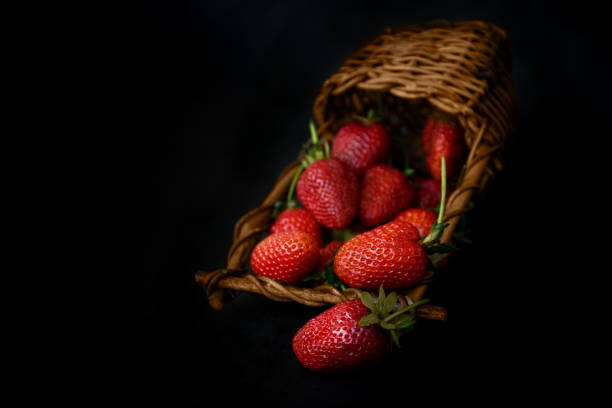 istock Ripe red strawberries scattered from wicker basket on black background 1323547864
