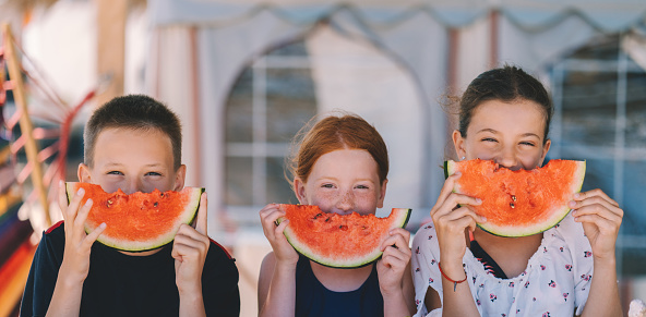 Three kids at the seaside eating sliced watermelon
