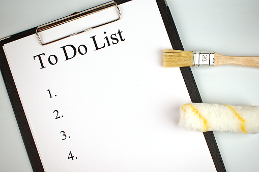 To do list. Notepad with a white sheet of paper, next to brush and roller on an white background. Renovation planning concept. Copy space. Flat lay.