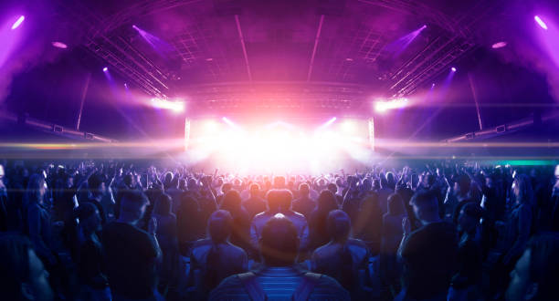 Concert spectators in front of a bright stage with live music Image shot during a music festival. Light comes from a stage with a band show, people silhouettes are visible in front of it. stage stock pictures, royalty-free photos & images