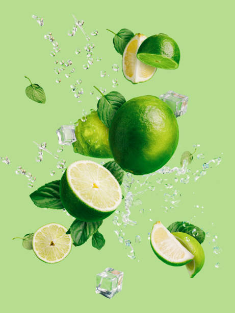 rodajas de cal fresca y madura con cubitos de hielo, salpicaduras de agua y hojas de menta lanzadas al aire, volando y levitando sobre un fondo verde brillante. concepto creativo de la comida. cítricos de verano. - limones verdes fotografías e imágenes de stock