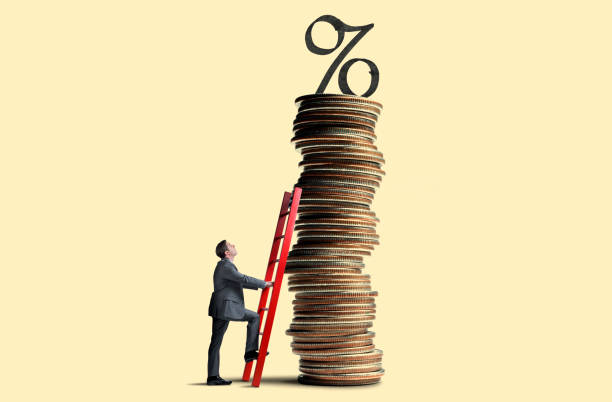 man leans ladder against tall stack of coins topped with interest rate symbol - inflation imagens e fotografias de stock