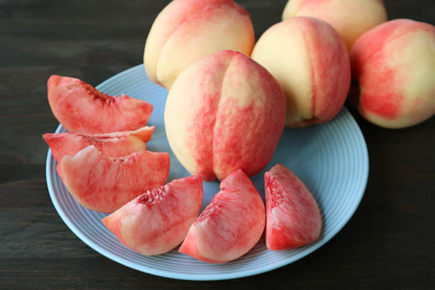Plate of Cut Fresh Ripe Peaches for Dessert with Blurry Whole Fruits in the Backdrop