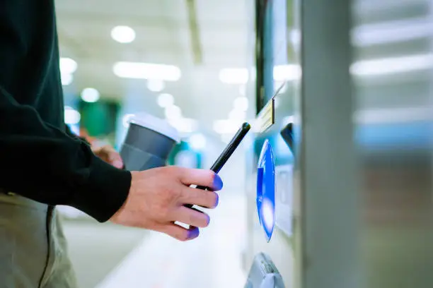 Photo of Close up of a young Asian man using contactless payment via smartphone to pay for her shopping at self-checkout kiosk in subway