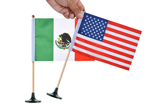 Hand placing American Flag in front of Mexican flag on white background