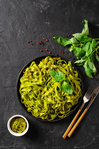 istock Green vegetarian basil pasta with pesto on black background 1323558508