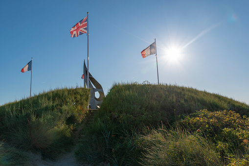 The Kieffer Commandos Monument stands tall, flanked by flags, in the late afternoon sun on Sword Beach in Ouistreham, France, one of the five D-Day landing beaches involved in Operation Overlord.