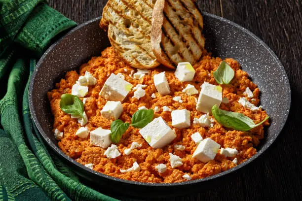 Strapatsada, eggs scrambled with tomatoes and feta cheese in a skillet with toasts, horizontal view, greek cuisine