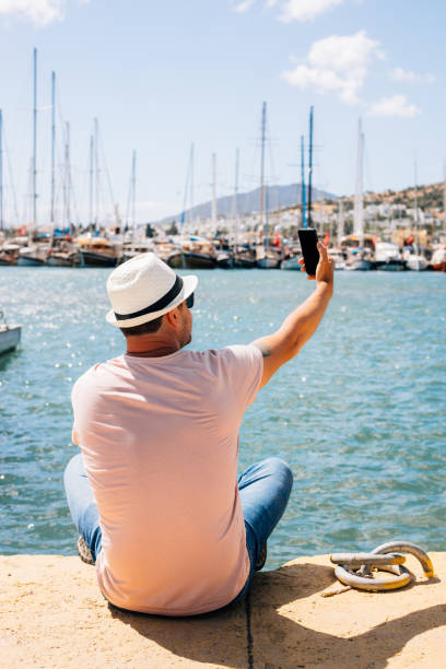 istock Man sitting at harbour, taking selfie 1323561342