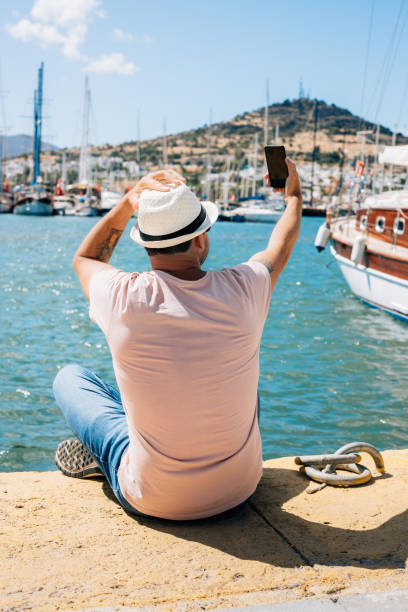 istock Man sitting at harbour, taking selfie 1323561577