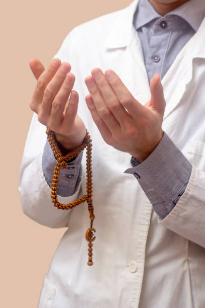 istock A young man in a white robe raised his hands up and prayed with a Muslim prayer beads. Beige background. Doctor praying. A Muslim makes dua. 1323566911