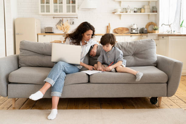 istock Young mother help son with homework on break from work on laptop computer from home. Family lockdown 1323567054