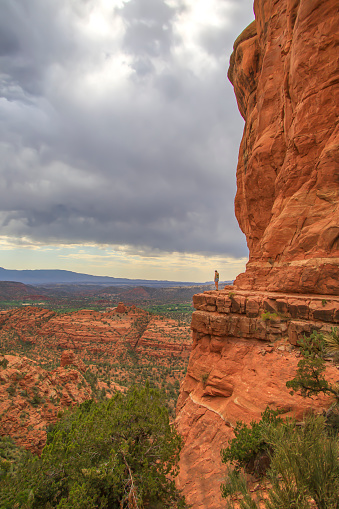 a picture of a Woman standing on a cliff next to red rocks