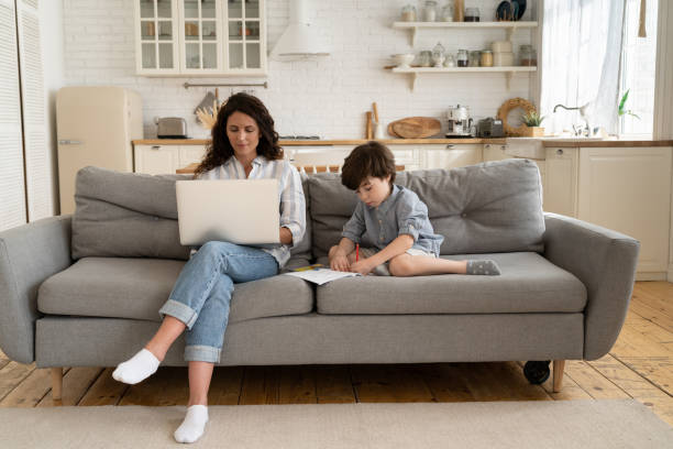 istock Working from home: mother freelancer use laptop computer sit on sofa together with small son drawing 1323567071