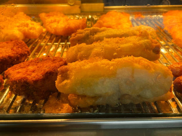 istock Close-up image of battered cod, haddock, sausages and fishcakes, fish and chip shop warming cabinet display with sliding door, focus on foreground 1323568222