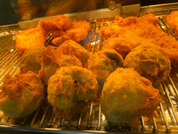 Close-up image of battered, mushy pea fritters, fish and chip shop warming cabinet display with sliding door, focus on foreground