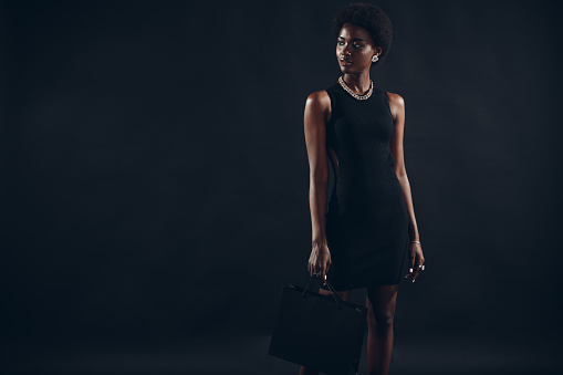 African american woman with afro hairstyle holds black shopping bags. Sale and discounts on market and Black Friday concept.