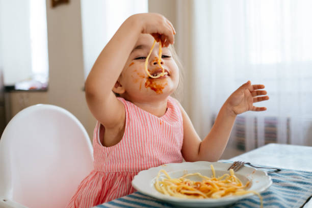 adorable petite fille mangeant des spaghettis à table - child eating pasta spaghetti photos et images de collection