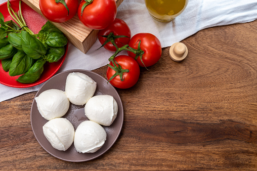 Cheese collection, small fresh white soft mozzarella cheese balls served with red tomatoes and fresh green basil from Italy close up