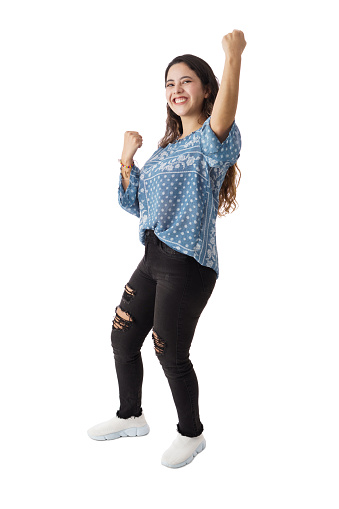 Side view of a joyful young latin woman raising her fists, celebrating and looking at the camera with a big smile.