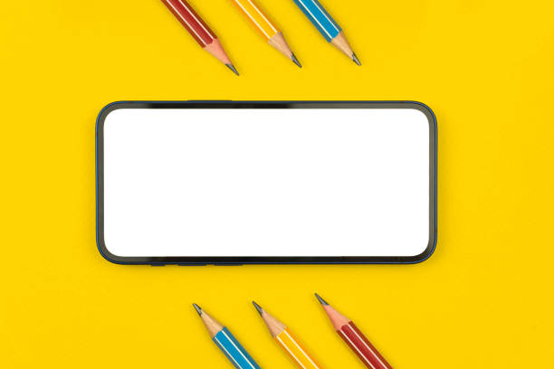 istock Mobile phone with school supplies flat lay composition with yellow desktop background, pencils on a table, top view photo with copy space 1323580400