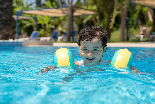 Cute little baby boy having fun in swimming pool, holiday resort