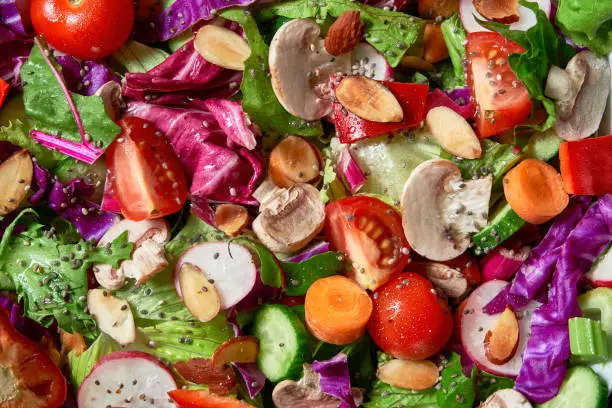 Top view of a colorful background of spring salad. Included ingredients: Olive oil, peppermint, chia, tomatoes, broccoli, lettuce, bell peppers, mushroom, carrots, radicchio and almonds.