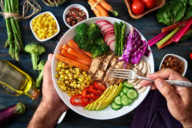 Healthy eating and diet concepts. Colorful and healthy fresh salad on rustic wood table. Included ingredients: Chicken, tomatoes, broccoli, lettuce, bell peppers, mushroom, carrots, radicchio, almonds.