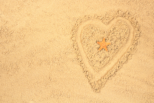 Silhouette of a heart on the background of a sandy beach, a starfish in the center. The concept of tourism, vacation, travel. Mock up for design with copy space, top view