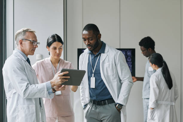 Group of Doctors at Medical Conference Waist up portrait of diverse group of doctors looking at digital tablet during council or conference african descent analyzing business white stock pictures, royalty-free photos & images