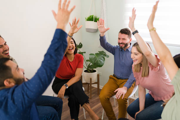 istock Diverse people laughing and raising their hands at group therapy 1323584327