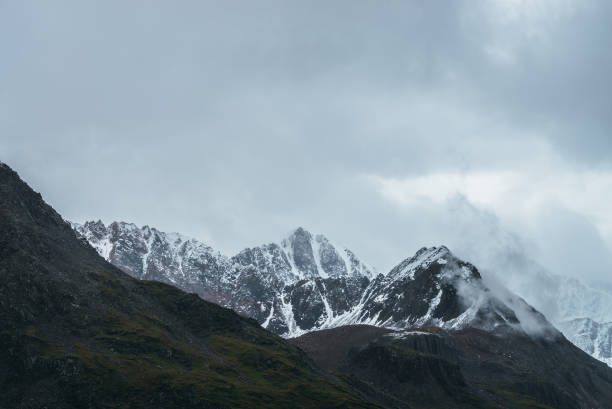 istock Atmospheric alpine landscape with great mountain peaked top with snow in low clouds. Dramatic mountain scenery with sharp pinnacle in overcast weather. Awesome view to snowy pointy peak in cloudy sky. 1323588007