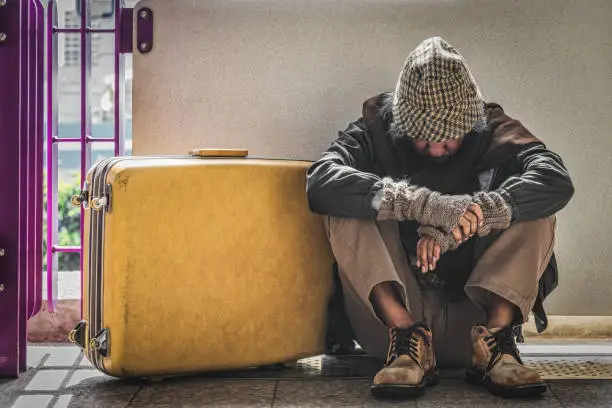 poor elderly homeless man sitting on pathway with luggage feel despair and lonely. concept of social proprem of poverty