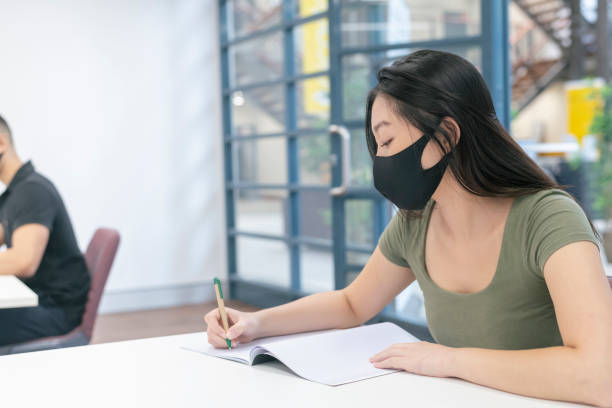 istock Young adult Asian woman wearing protective face mask while attending class 1323601646