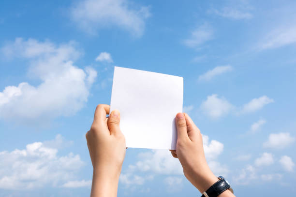 Woman hand holding white paper with sky and cloud background.