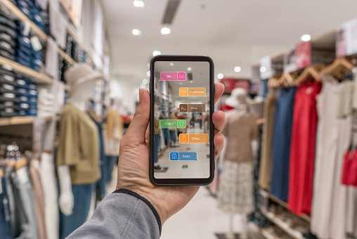 Augmented reality marketing . Hand holding smart phone use AR application to check information in a large clothing shop