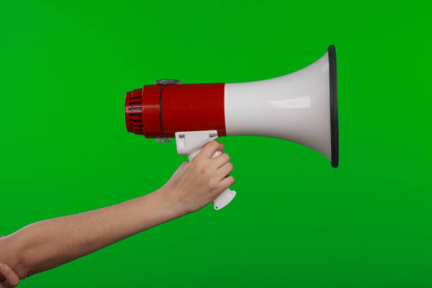 istock A woman's hand holds a loudspeaker on a green background isolated object 1323610590